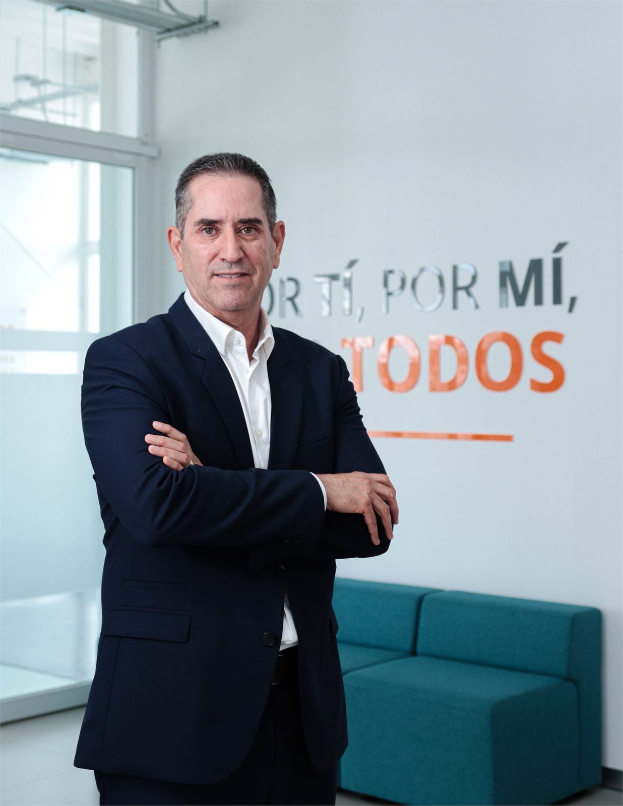 Retrato corporativo con los brazos cruzados frente al lema «Por ti, por mí, por todos» de Minas de San Nicolás