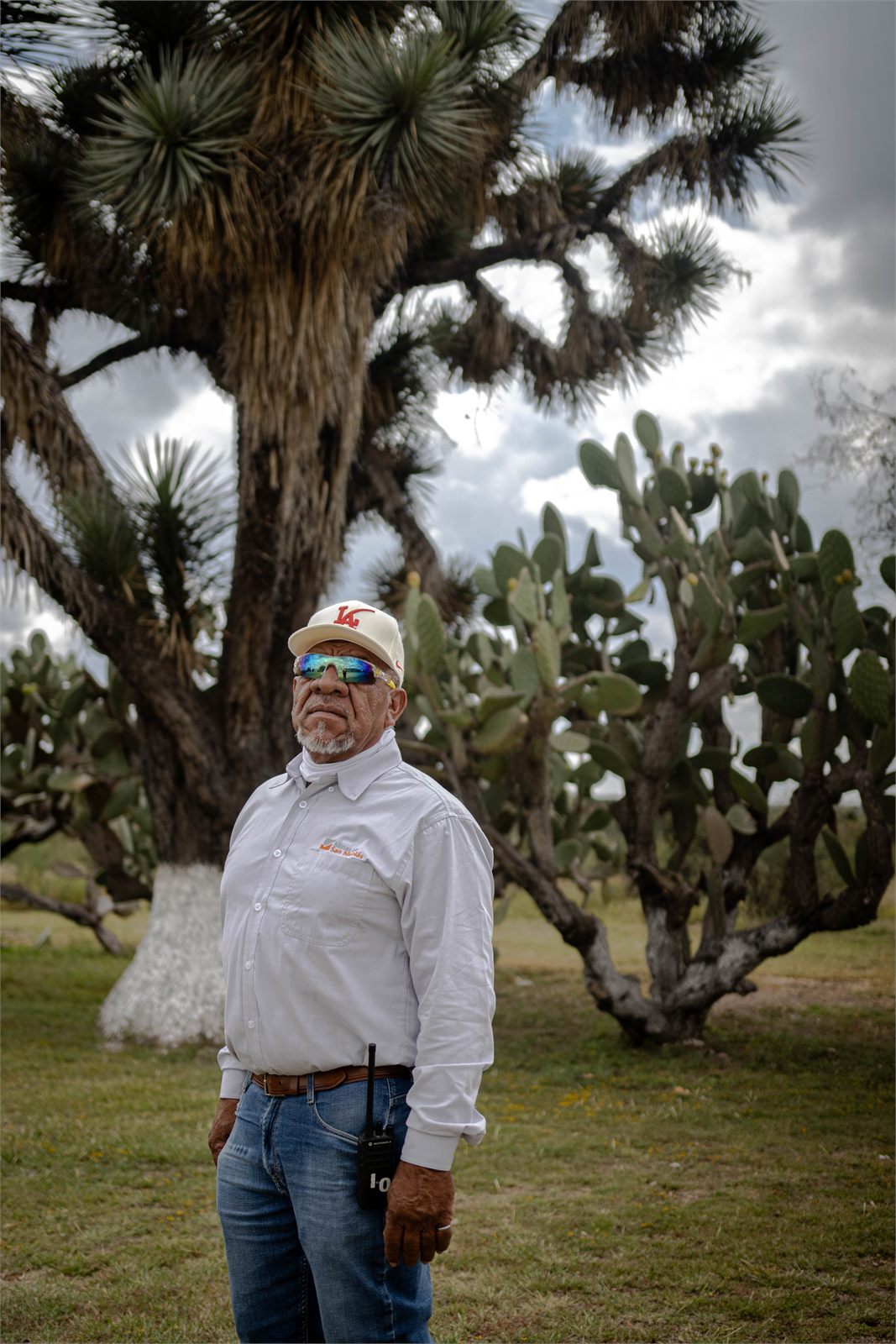 Retrato en exteriores junto a una yuca y nopales, con gorra y camisa de trabajo