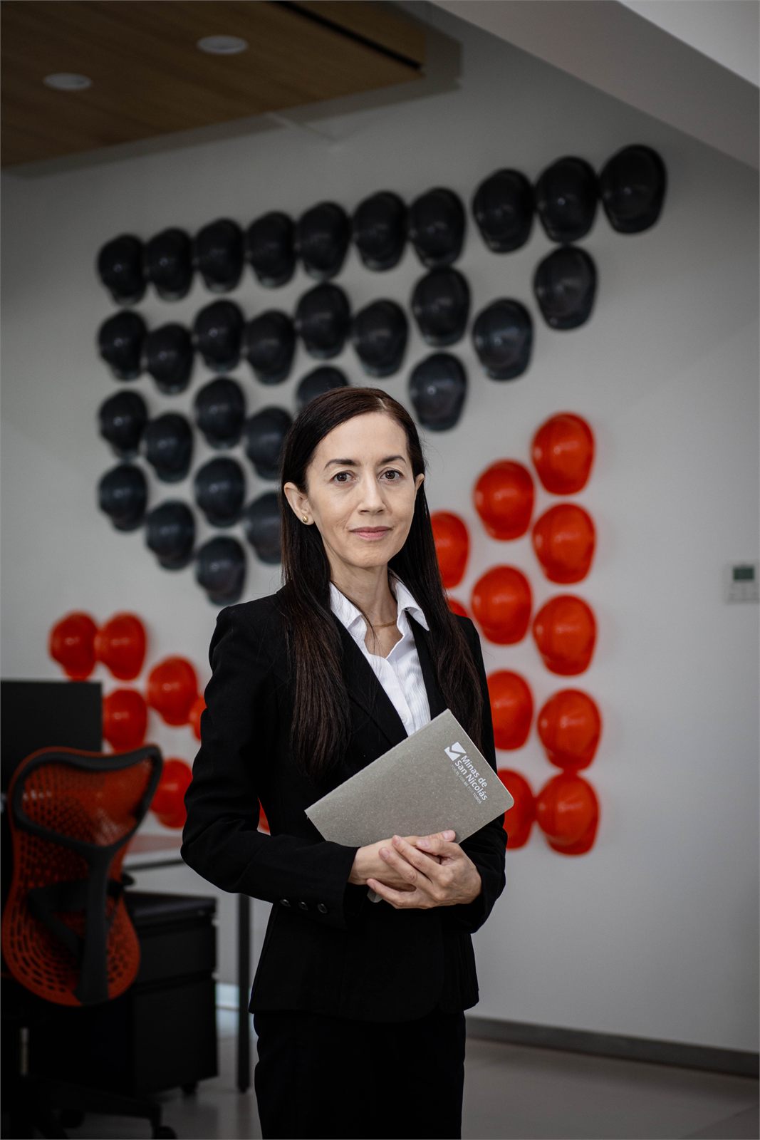 Retrato corporativo con carpeta frente al muro de cascos de seguridad