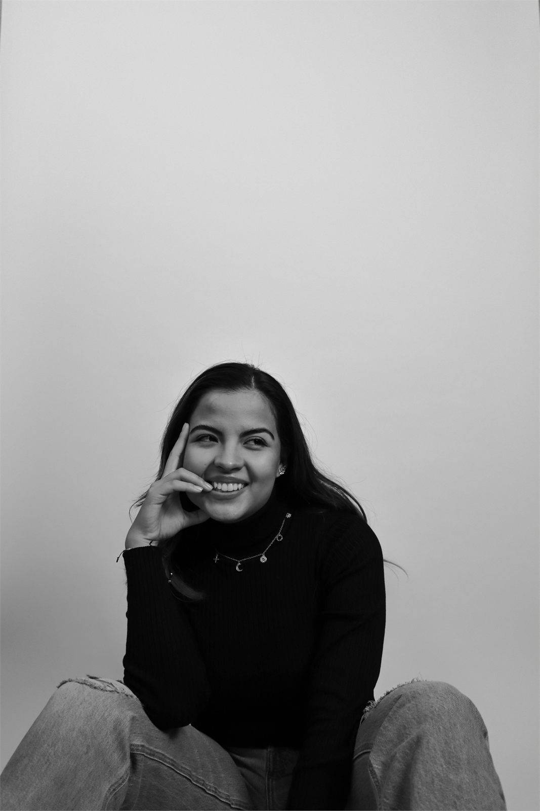 Retrato de estudio en blanco y negro, sentado con la mano en el rostro y sonriendo